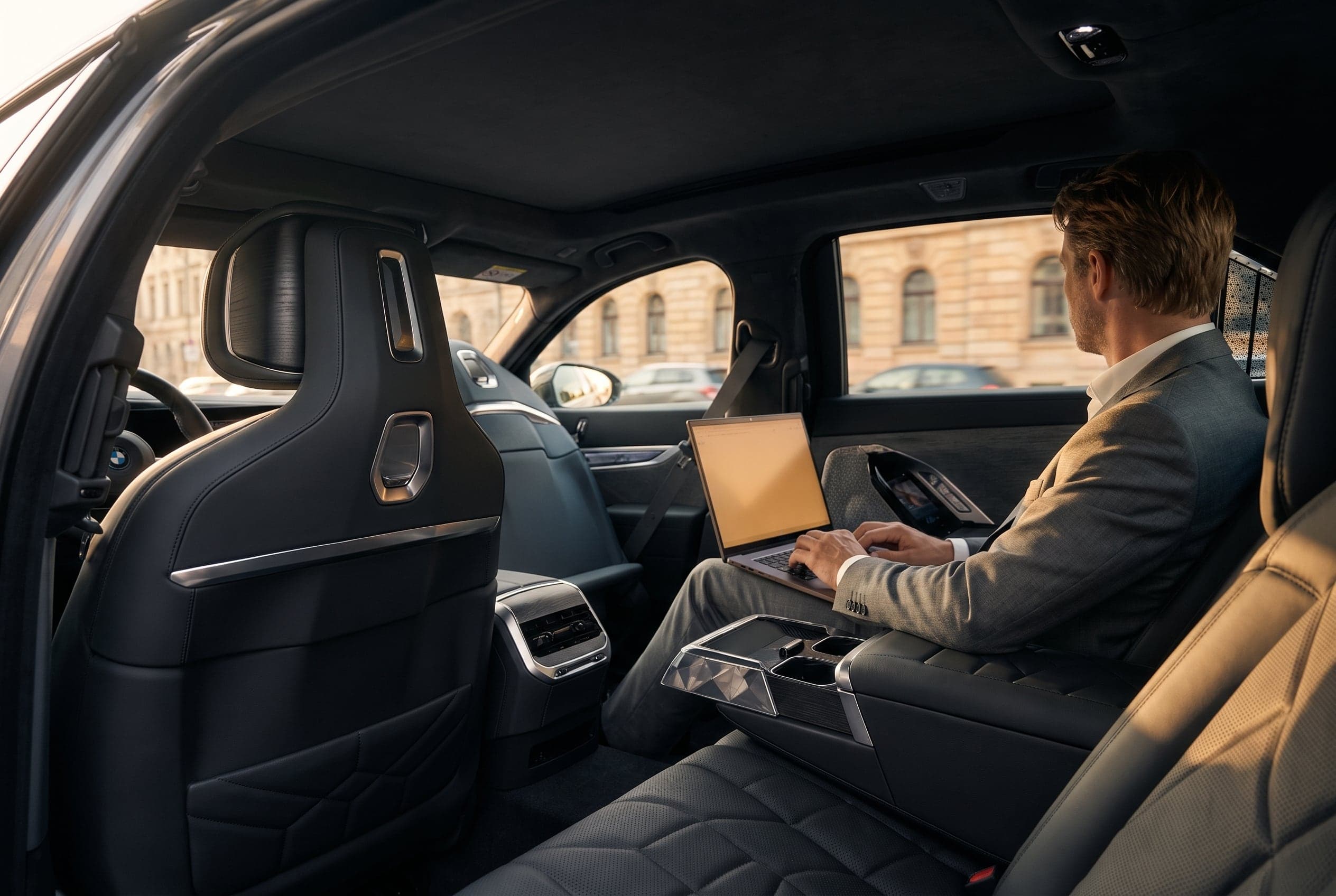 A passenger in a suit working on a laptop in the BMW i7's rear cabin with a classical building visible through the window.